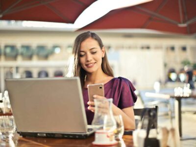 Woman looking at a phone while sitting in front of a laptop