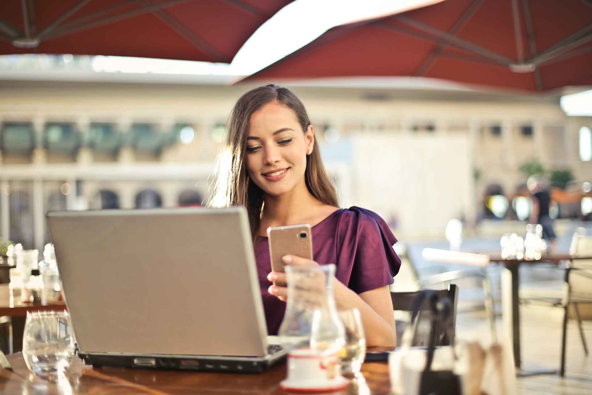 Woman looking at a phone while sitting in front of a laptop